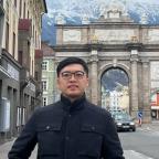 Jonathan Wong standing in front of a monument and mountain on a city street.